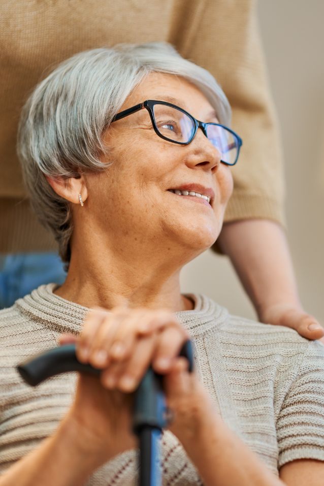 Smiling senior women with cane with a supportive caregiver behind her