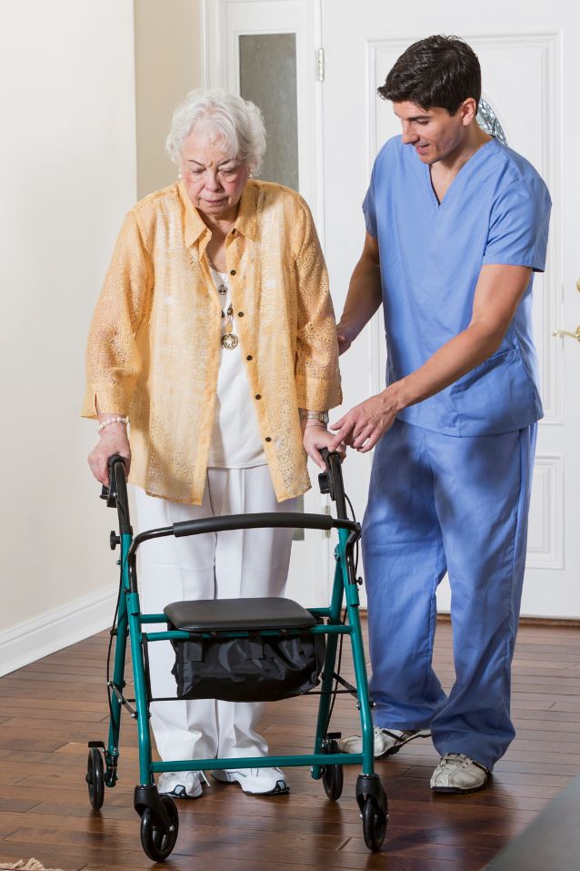 Caregiver assisting an older woman walk with a wheeled walker