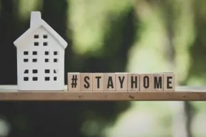 A small house figurine next to wooden blocks spelling Stay Home, promoting home safety and health precautions.