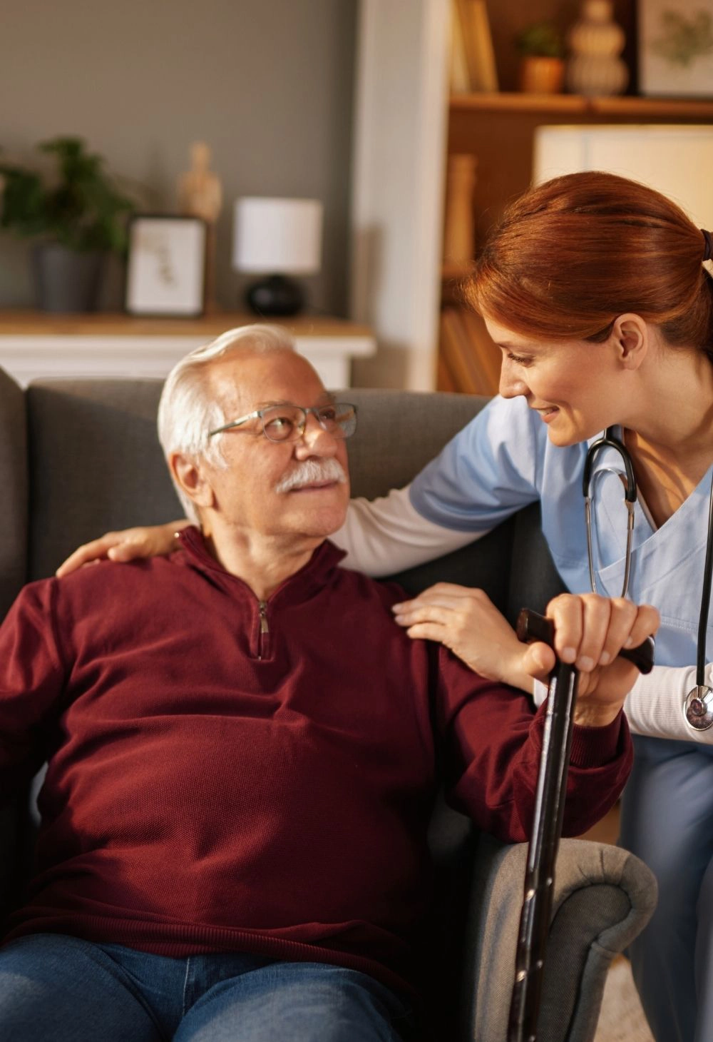 A nurse helps a senior man sit comfortably and provides supportive in-home care.