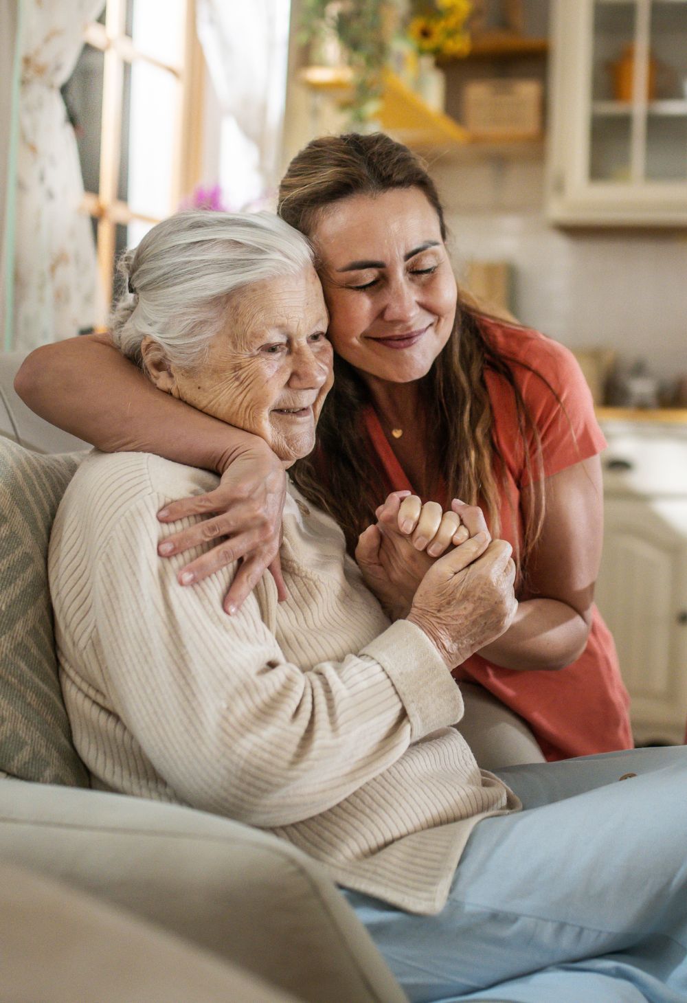Caregiver warmly hugging an elderly woman while sitting on the couch highlighting hospice care.