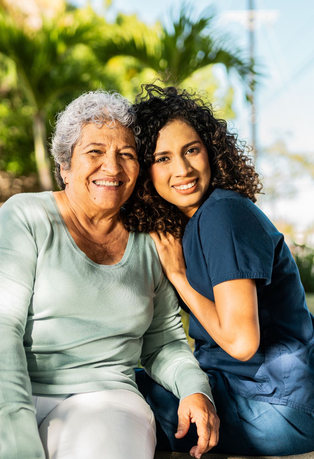 A caregiver hugging an elderly woman while happily sitting together.