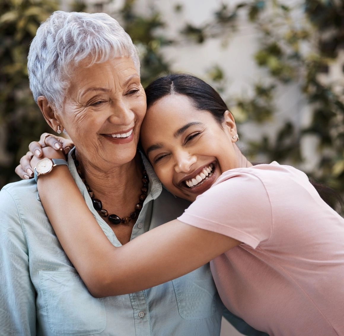 A happy caregiver hugging a smiling senior woman in an outdoor setting, highlighting loving companionship and in home support.