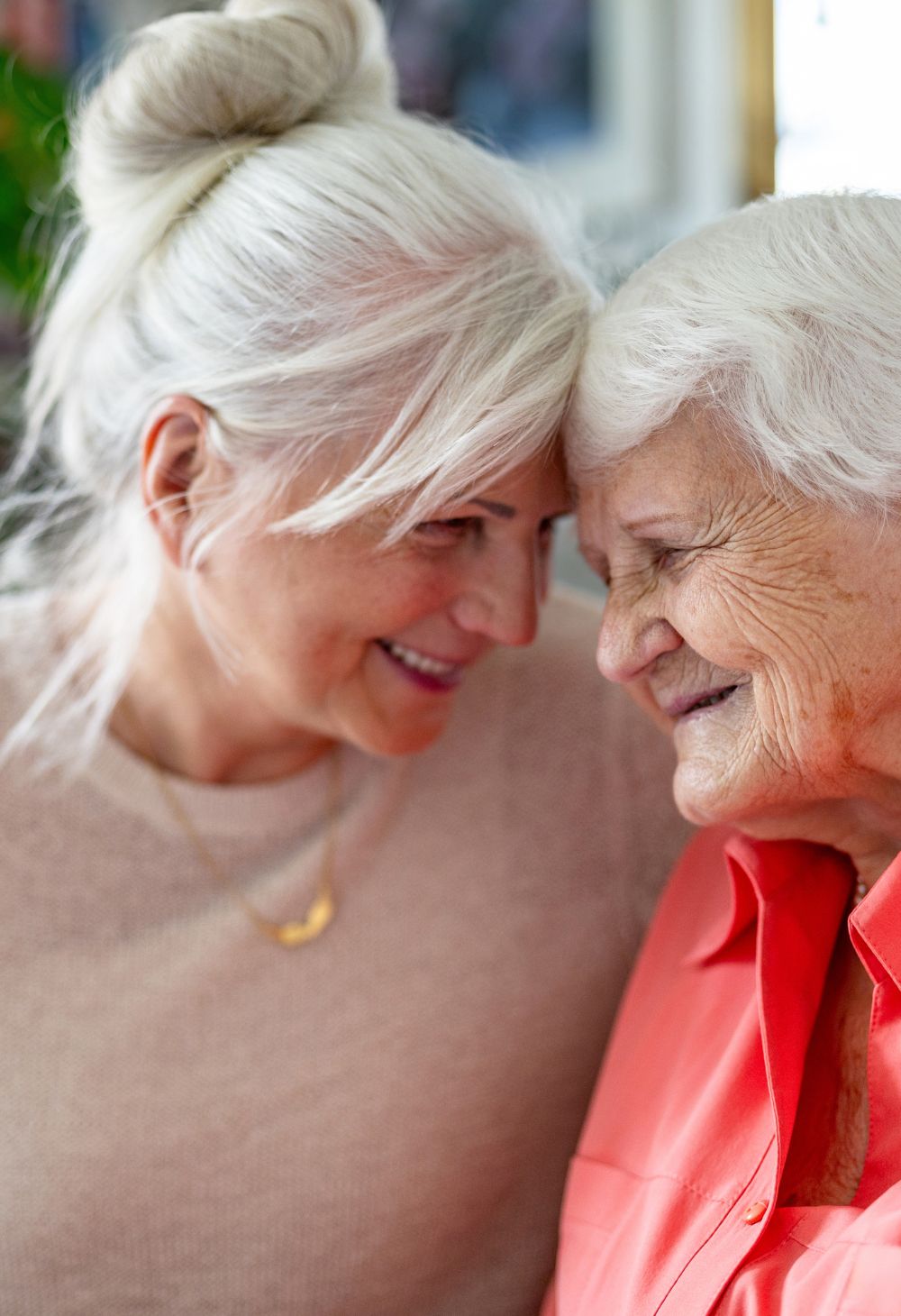 Caregiver and senior woman sharing a tender moment with their foreheads touching and smiling warmly