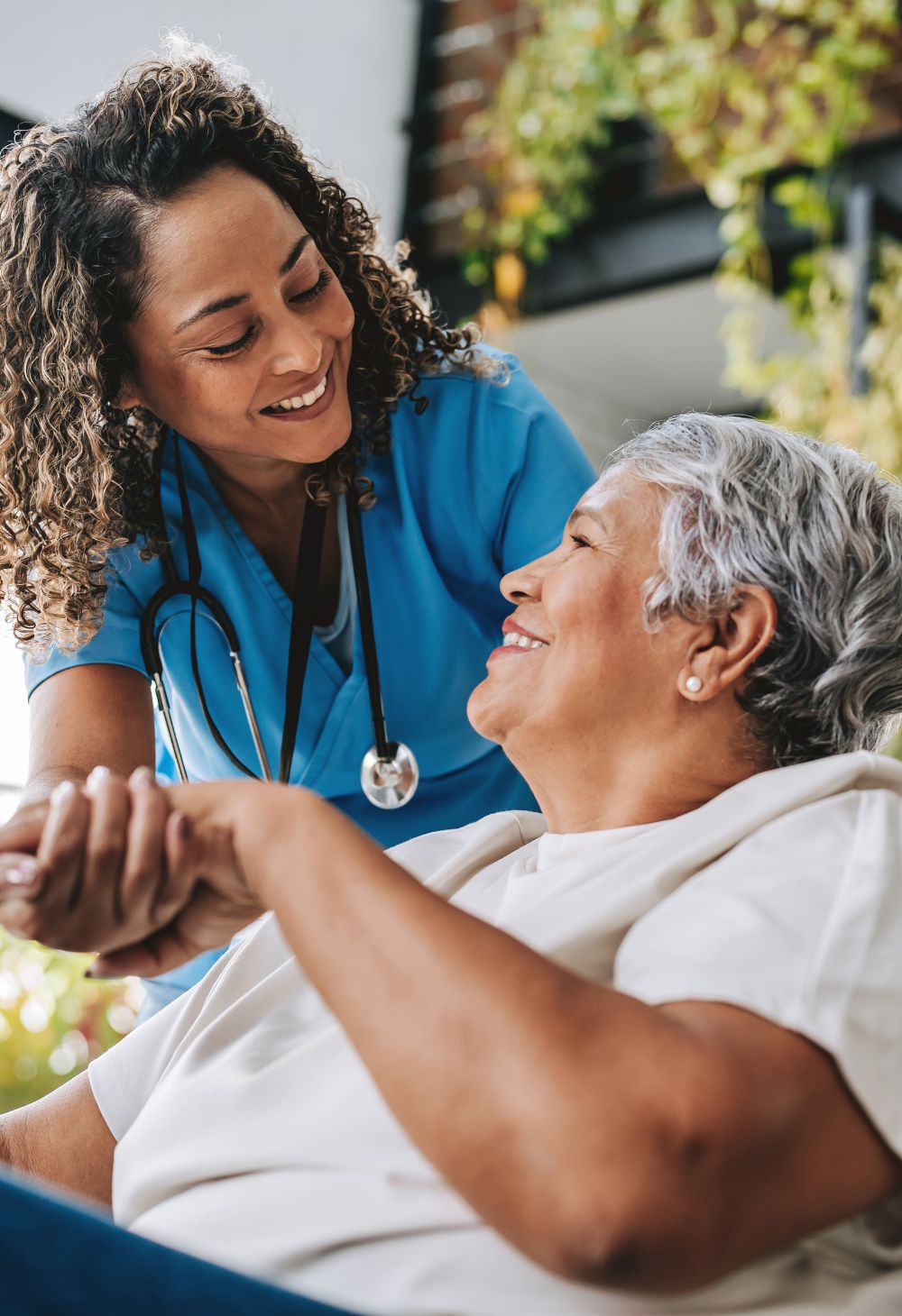 Caregiver Supporting a Senior Woman Nurse in blue scrubs gently holding the hand of an older woman while they smile at each other during in-home care
