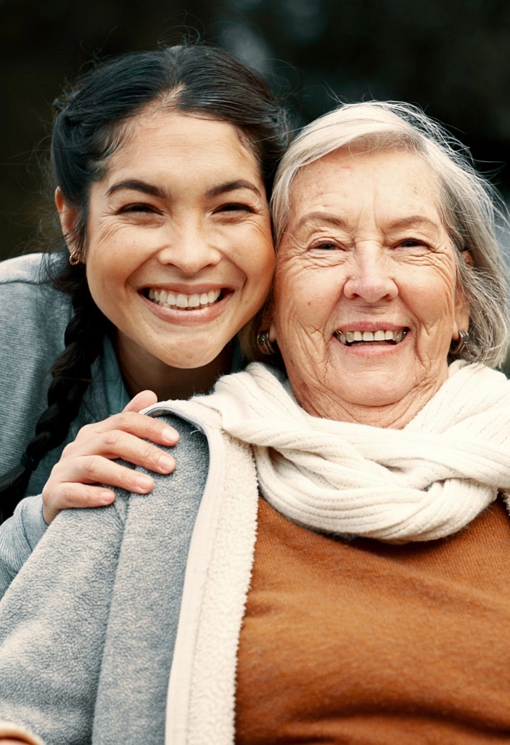 A caregiver smiling and hugging a senior woman during a happy moment outdoors.
