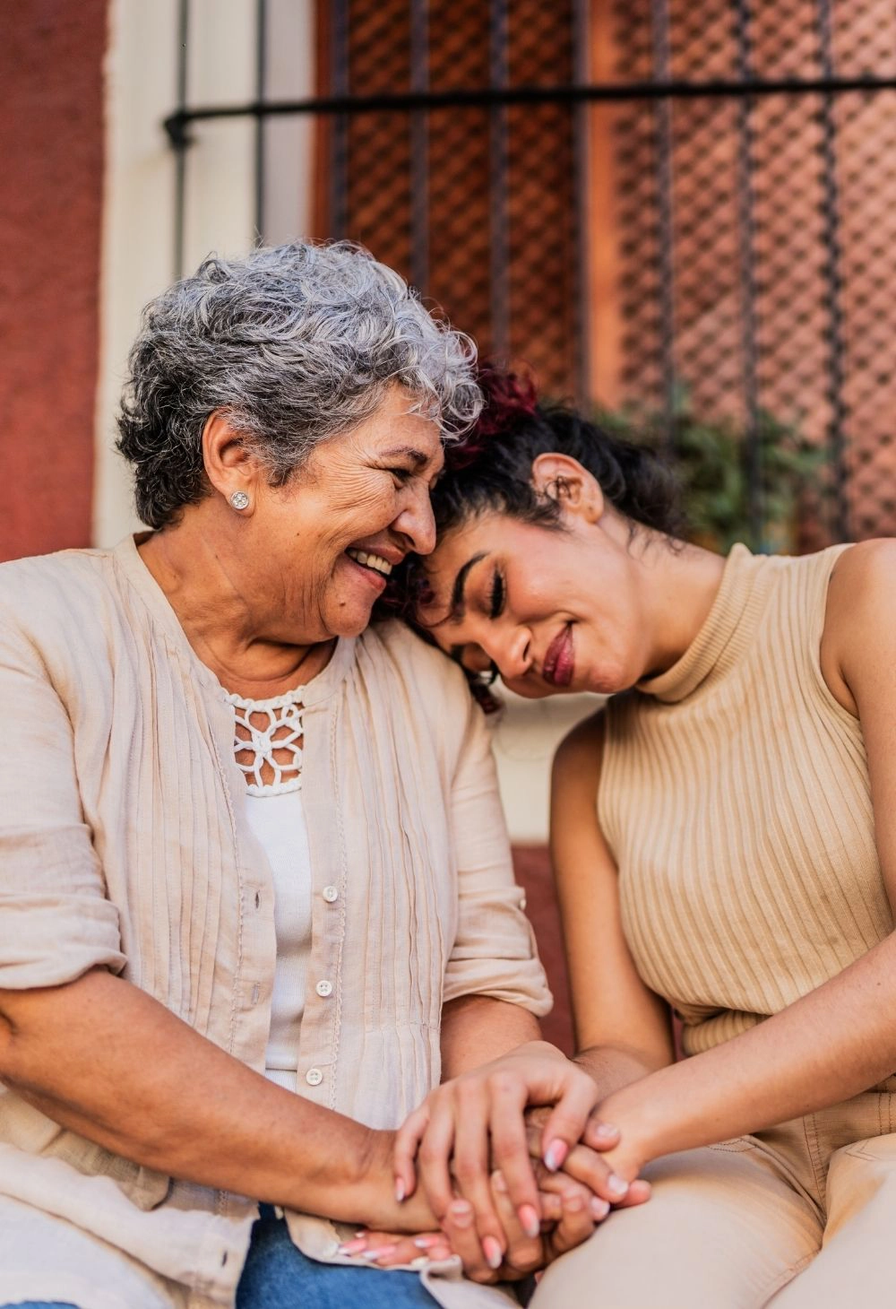 A caregiver gently holding hands with a senior woman as they smile together.