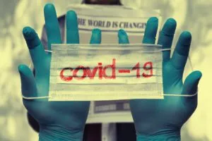 A pair of hands wearing medical gloves holding up a face mask labeled Covid nineteen, symbolizing safety precautions and pandemic awareness.
