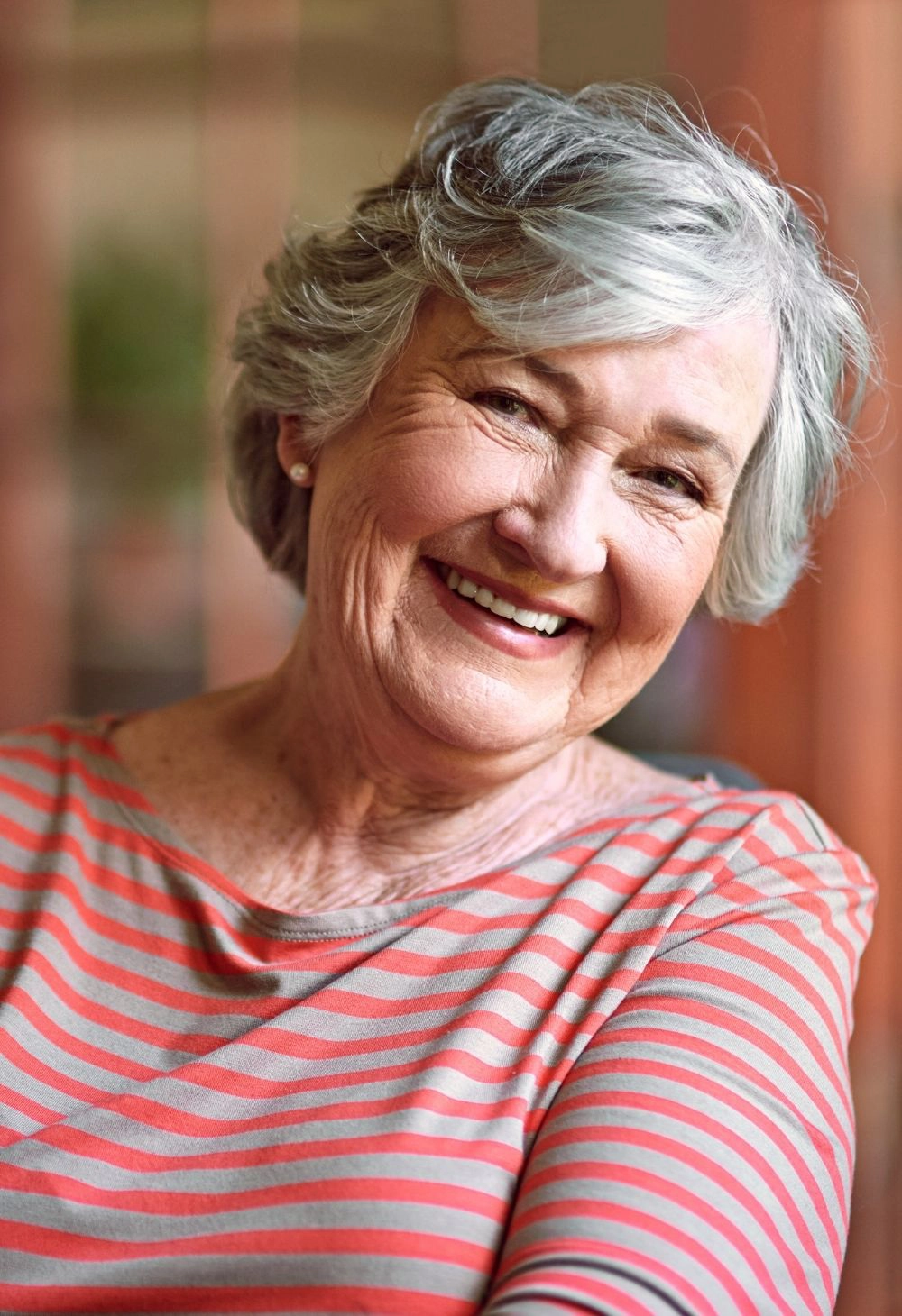 A joyful senior woman smiling while sitting comfortably in a bright room.