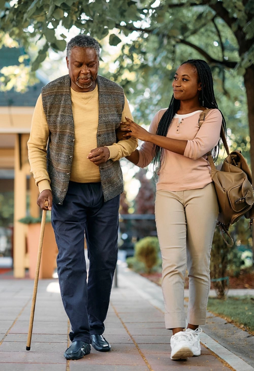 A caregiver assisting an elderly man with a cane during a peaceful outdoor walk.