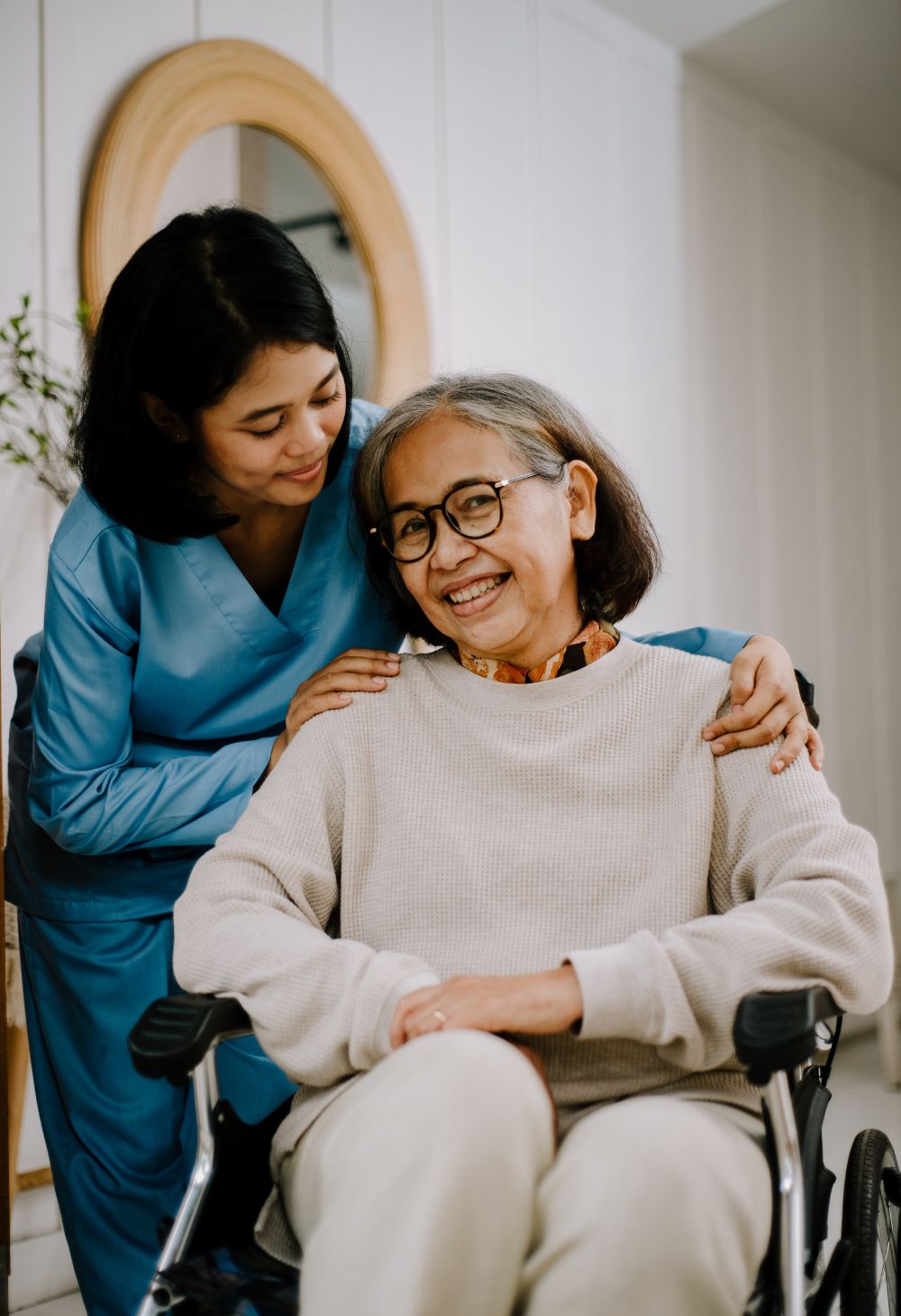 Caregiver standing beside an elderly woman in a wheelchair, offering supportive in-home care