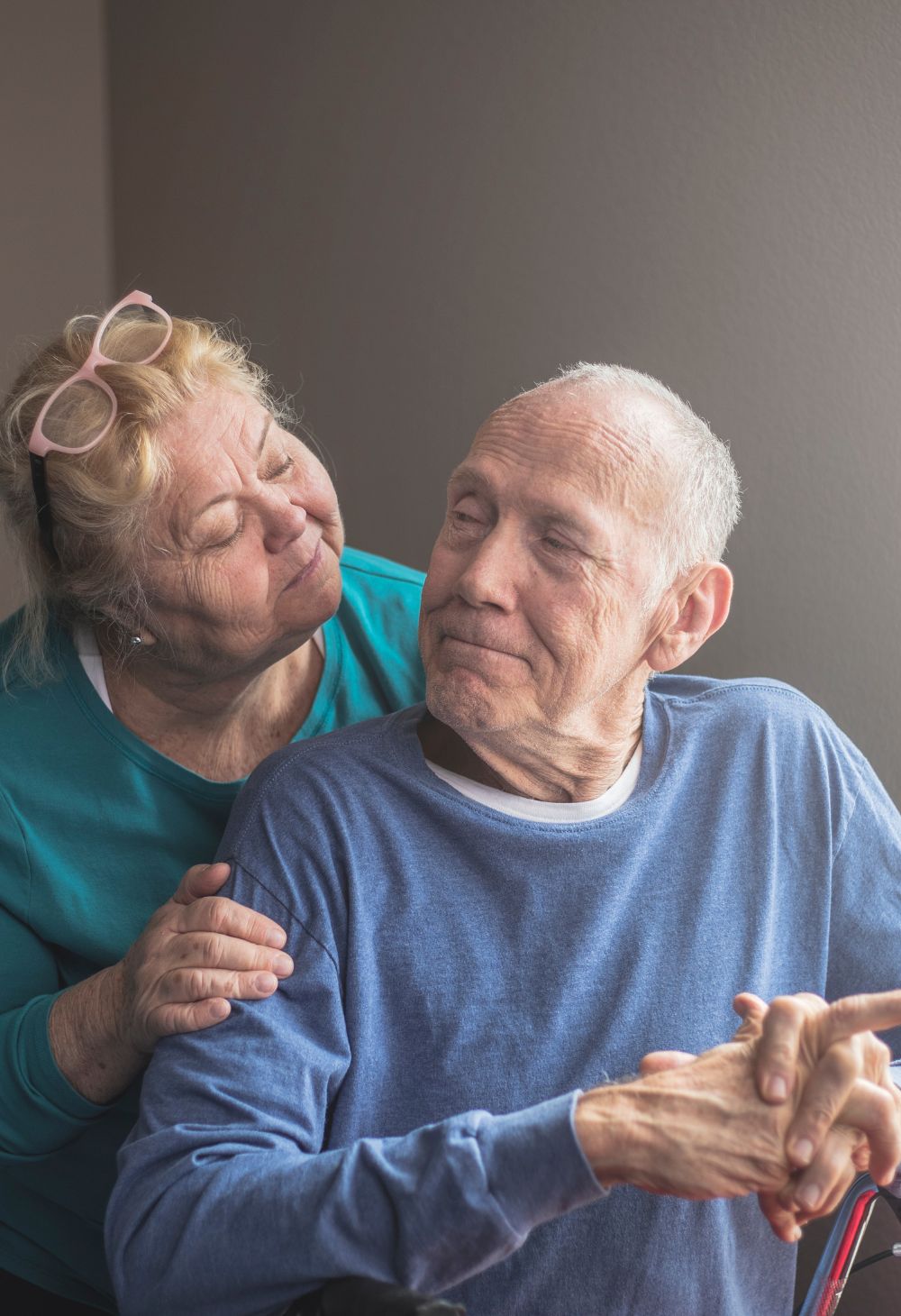 Older woman offering comfort to an elderly man at home, showing supportive senior care