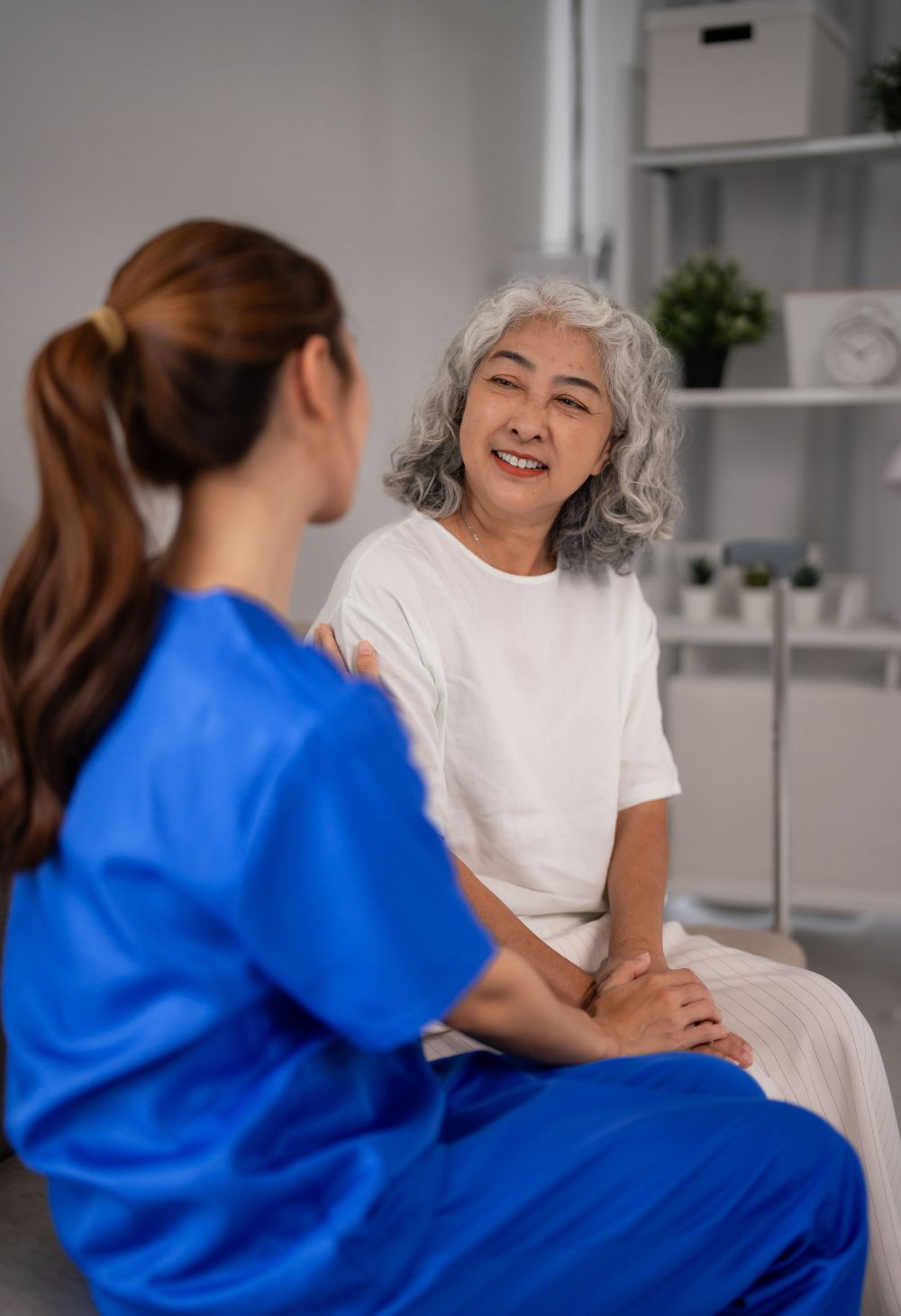 Caregiver in blue scrubs speaking with an elderly woman, providing emotional support during an in-home care visit