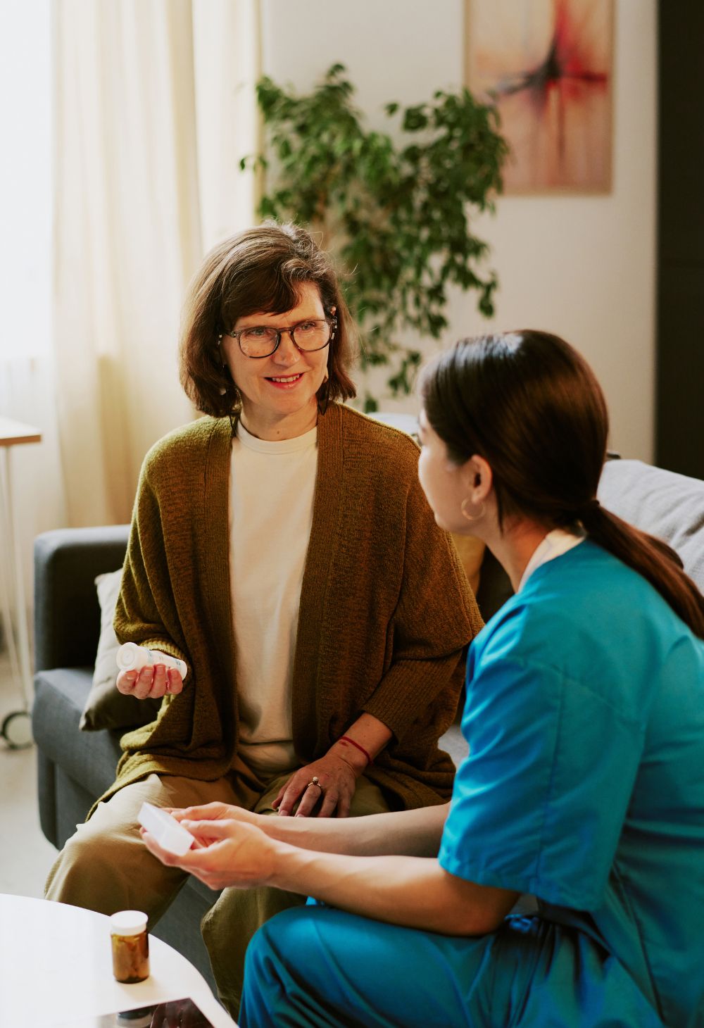 A caregiver in blue scrubs assisting a senior woman with her medication during an in-home visit.