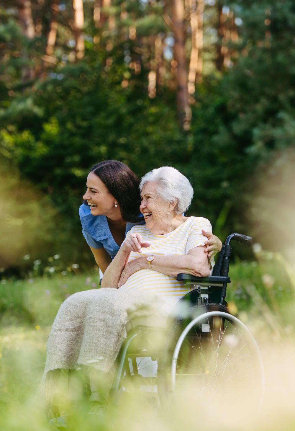 Caregiver Supporting Senior in a Wheelchair Outdoors in San Marcos A smiling caregiver leans beside an older woman in a wheelchair during a peaceful outdoor outing.