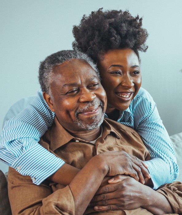 A smiling caregiver affectionately hugging an elderly man from behind, illustrating dedicated companionship care in Escondido, CA.