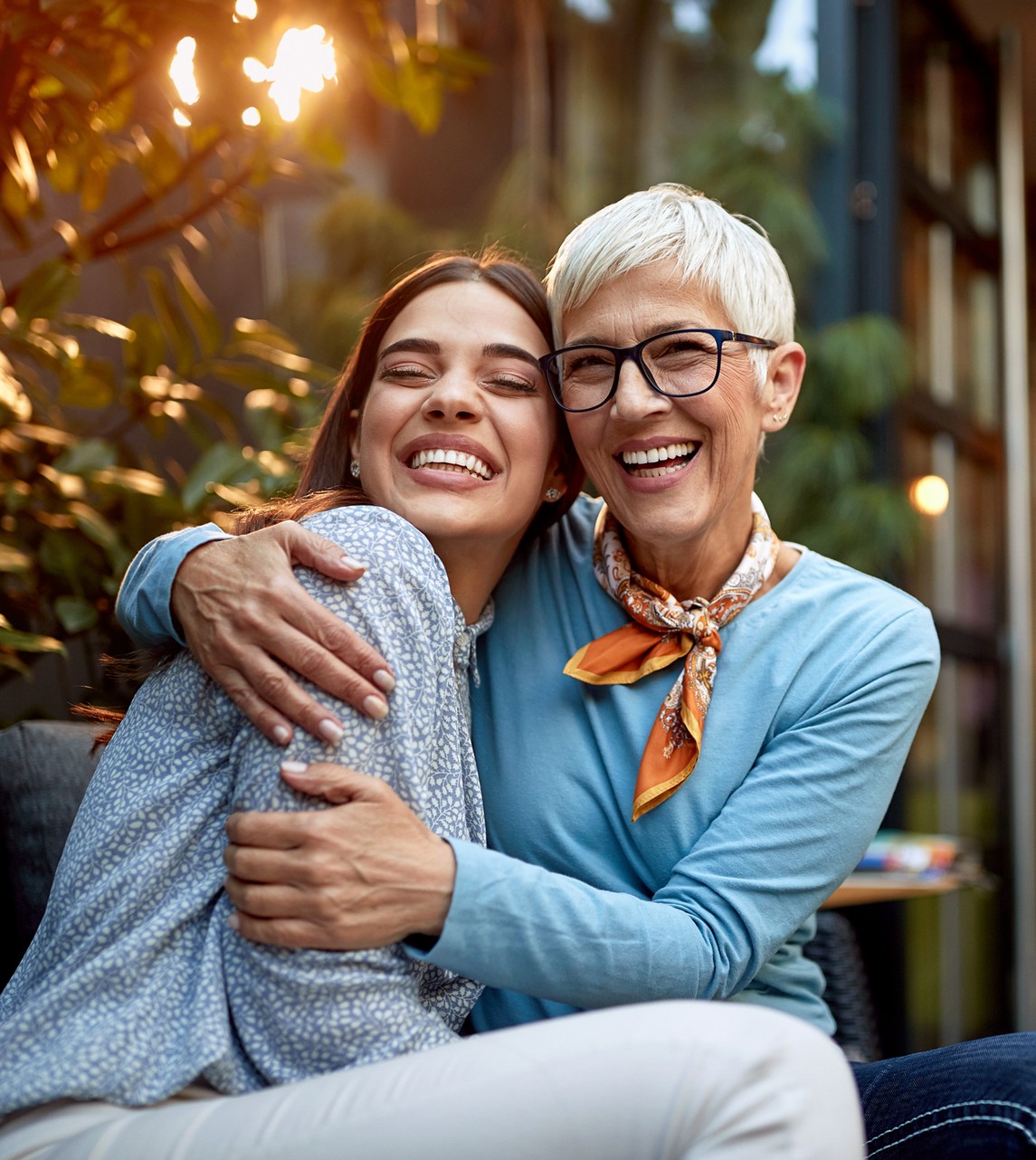 A joyful younger caregiver and a smiling senior woman with white hair sharing a warm hug outdoors, representing reliable companionship care in Escondido, CA.